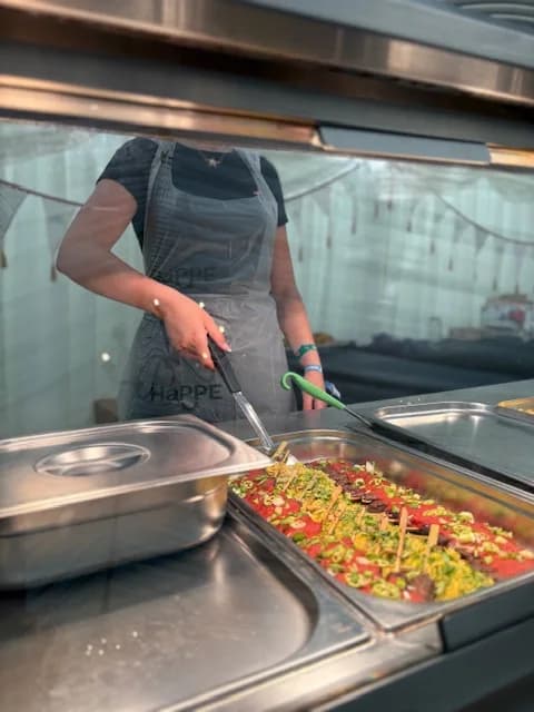A kitchen worker wearing a HaPPE compostable apron serving from a hot counter